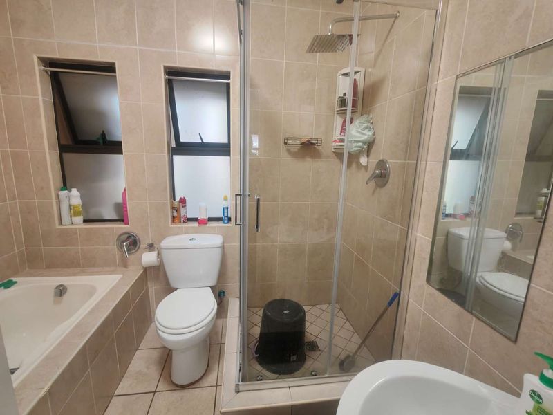 A functional bathroom featuring a built-in bathtub, a separate glass-enclosed shower with a rain shower head, and neutral wall and floor tiling.