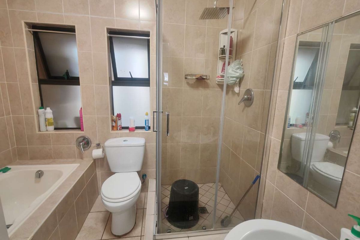 A functional bathroom featuring a built-in bathtub, a separate glass-enclosed shower with a rain shower head, and neutral wall and floor tiling.