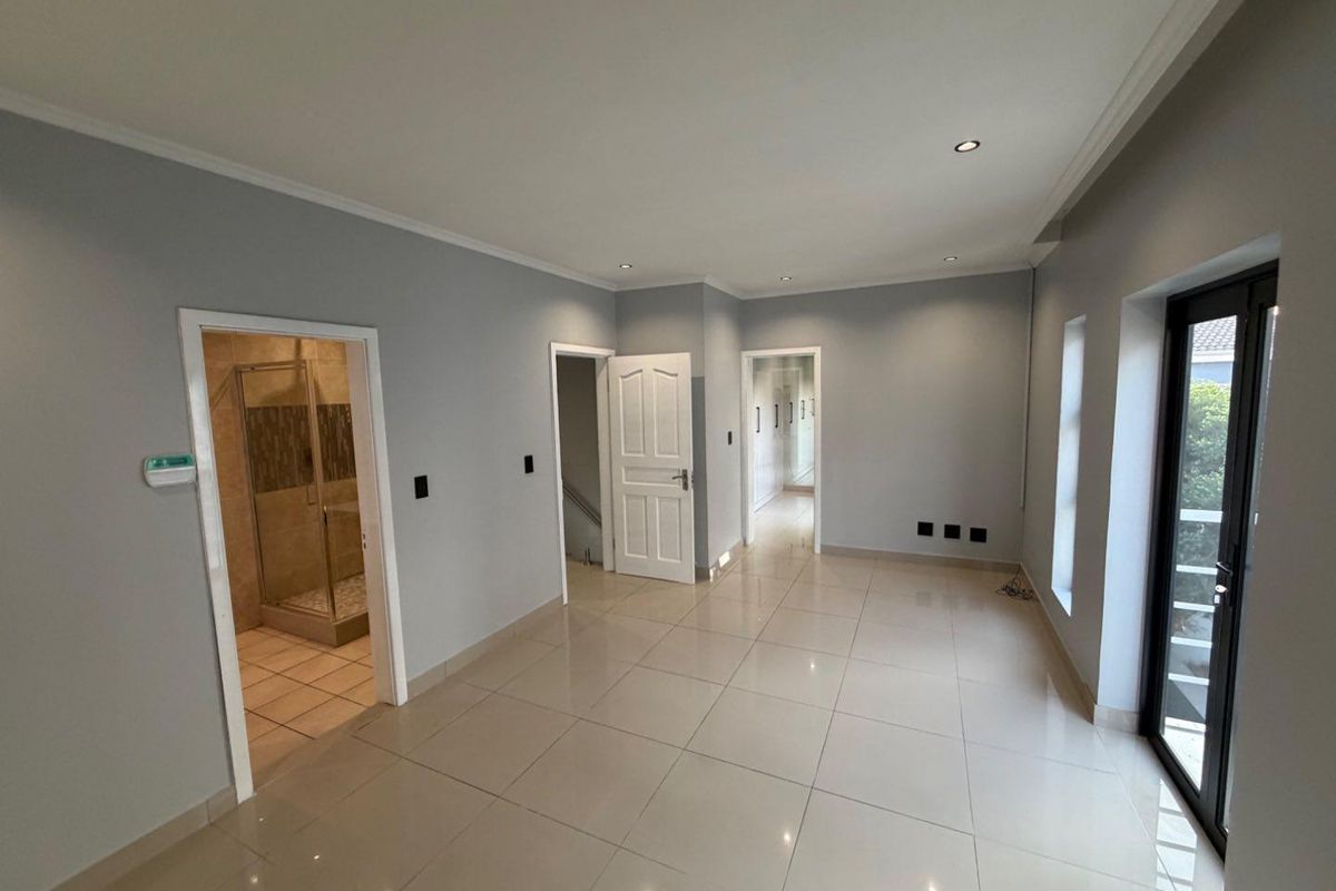 A bright, empty living area featuring neutral tiled flooring, recessed lighting, and direct access to an outdoor space, with an adjacent en-suite bathroom.