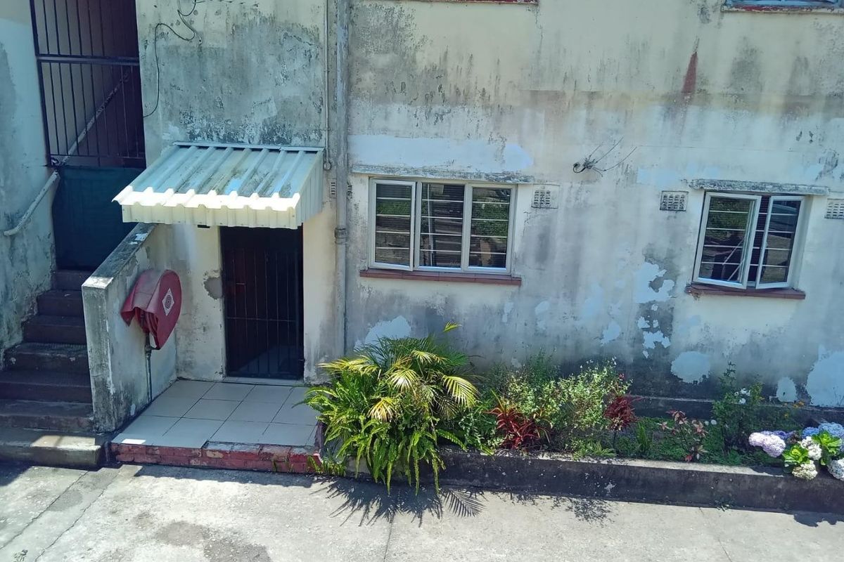 Exterior view of an apartment building rear facade showing a ground floor entrance, security gate, and weathered concrete walls requiring maintenance.