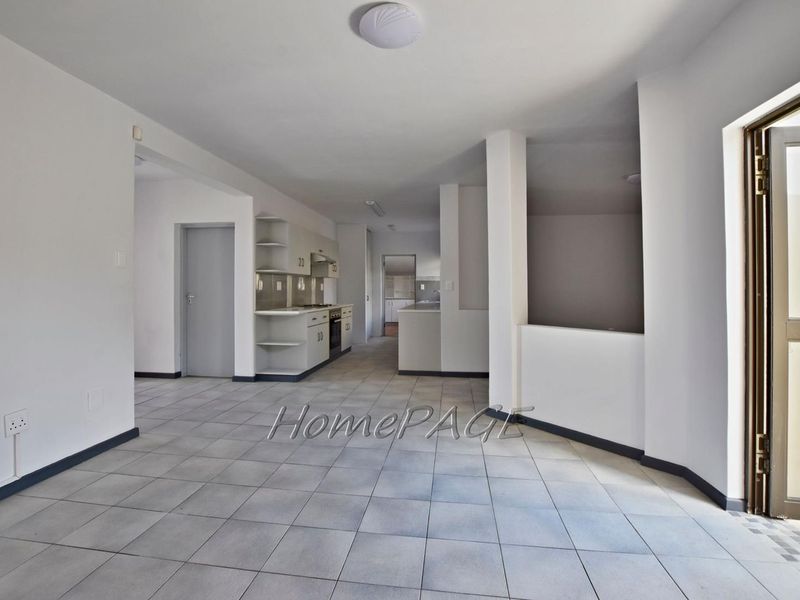 Spacious open-plan living area featuring tiled flooring and a functional kitchen with built-in cabinetry, oven, and hob.