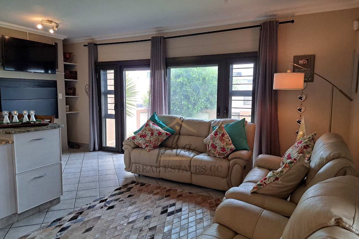 A comfortable living room featuring tiled flooring, large sliding glass doors providing natural light, and built-in shelving units.