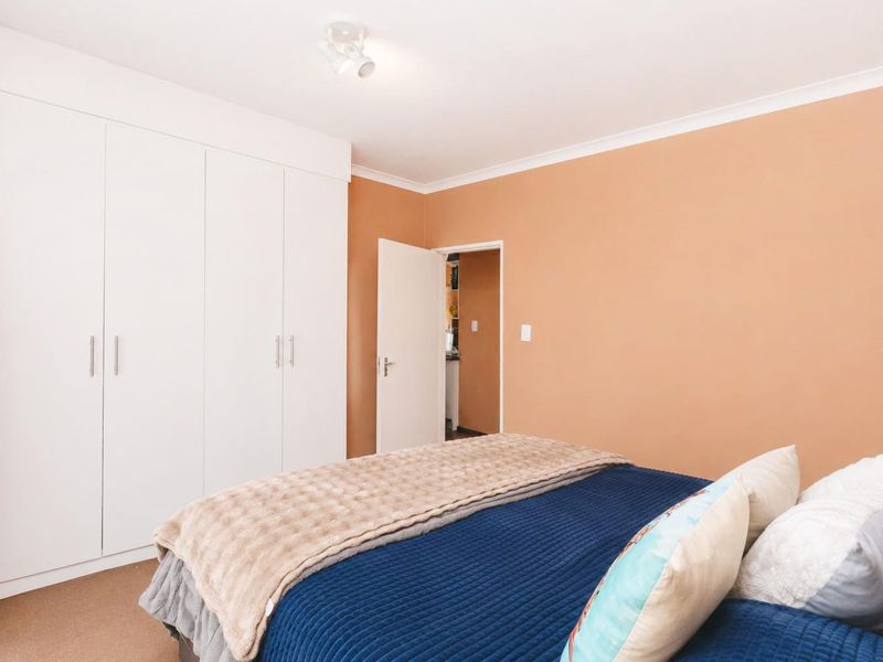 A bedroom featuring built-in cupboards, neutral carpeting, and warm-toned walls, offering a functional and comfortable living space.