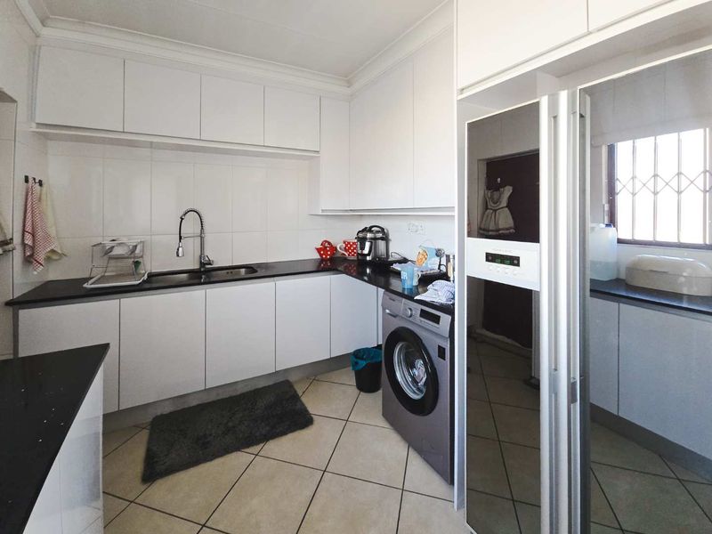 A functional kitchen featuring white cabinetry, dark stone countertops, tiled backsplash, and tiled flooring with integrated space for laundry appliances.