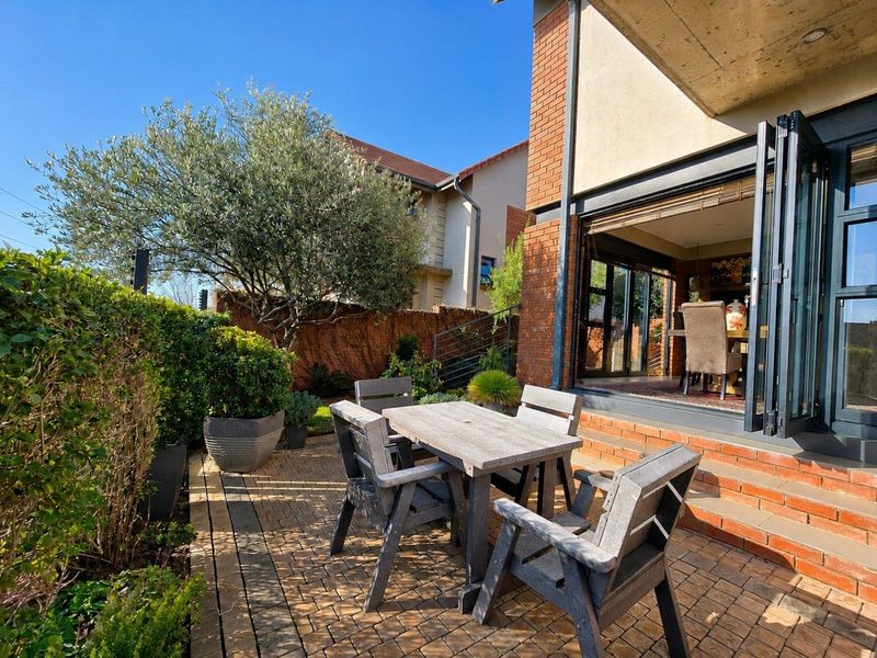 A paved outdoor patio area featuring bi-fold doors that open into the interior living space, complemented by a brick facade and exposed concrete ceiling.