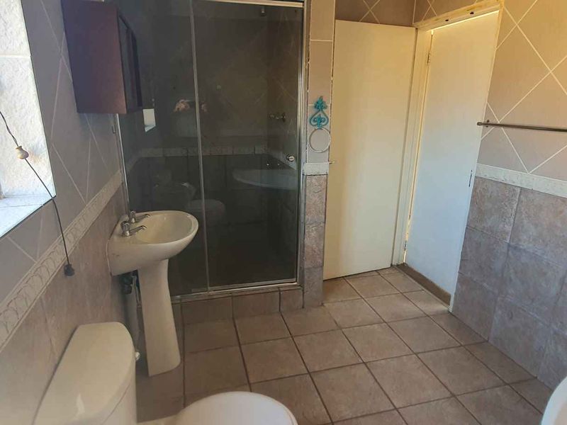 A functional bathroom featuring a pedestal basin, toilet, and a glass-enclosed shower with tiled walls and flooring.