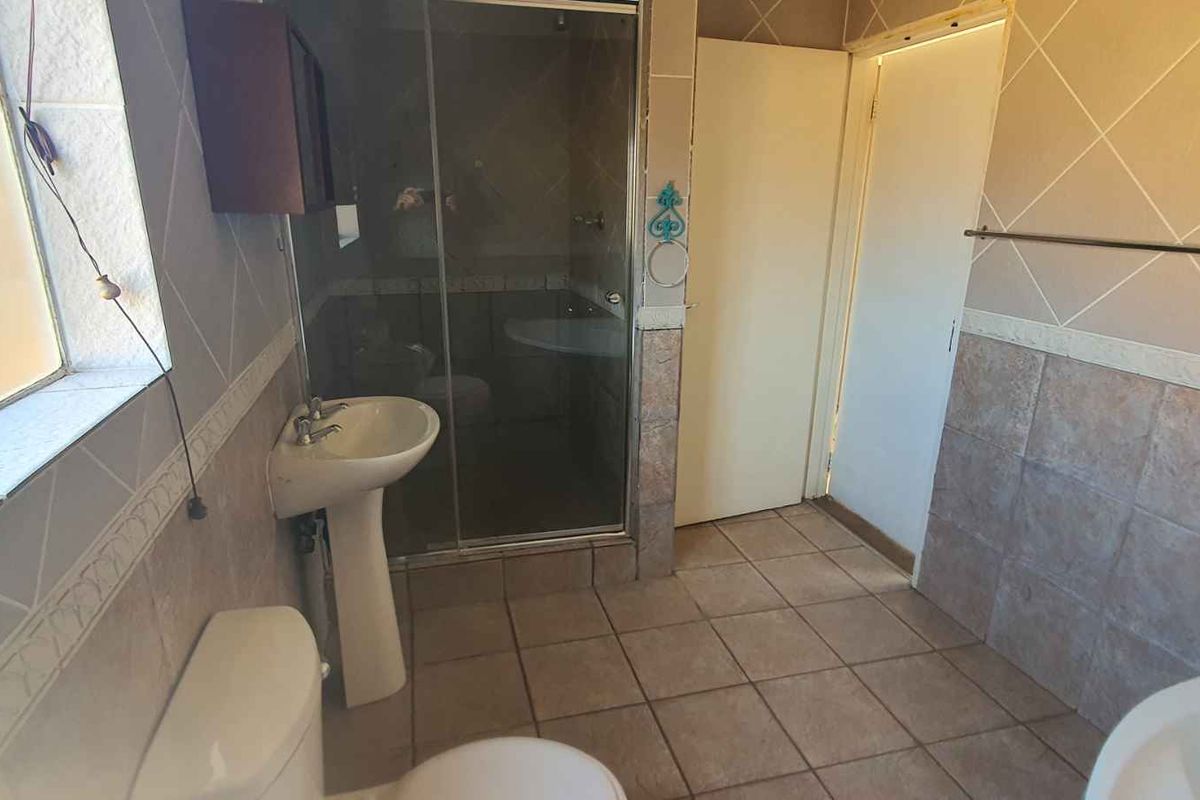 A functional bathroom featuring a pedestal basin, toilet, and a glass-enclosed shower with tiled walls and flooring.