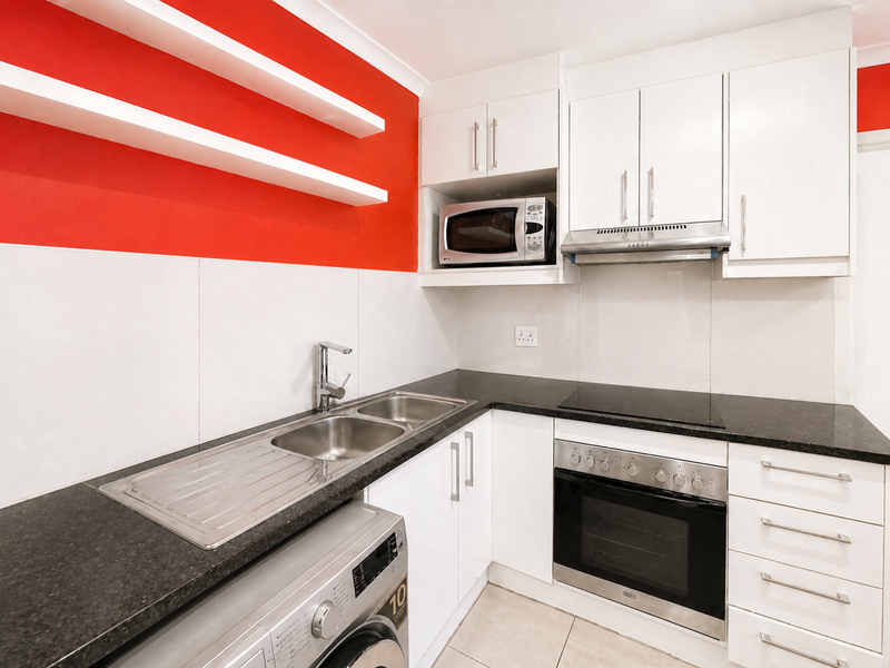 Modern kitchen featuring white cabinetry, granite countertops, built-in oven, hob, extractor fan, and integrated microwave with a vibrant red accent wall.
