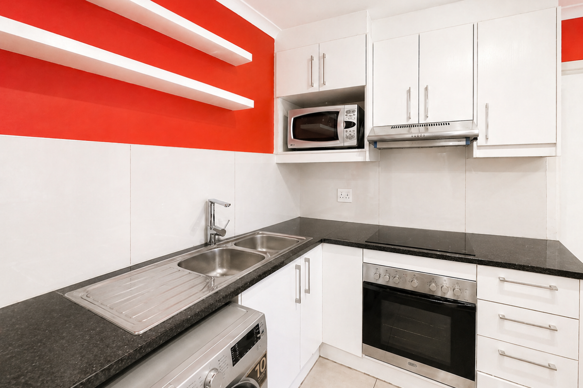 Modern kitchen featuring white cabinetry, granite countertops, built-in oven, hob, extractor fan, and integrated microwave with a vibrant red accent wall.