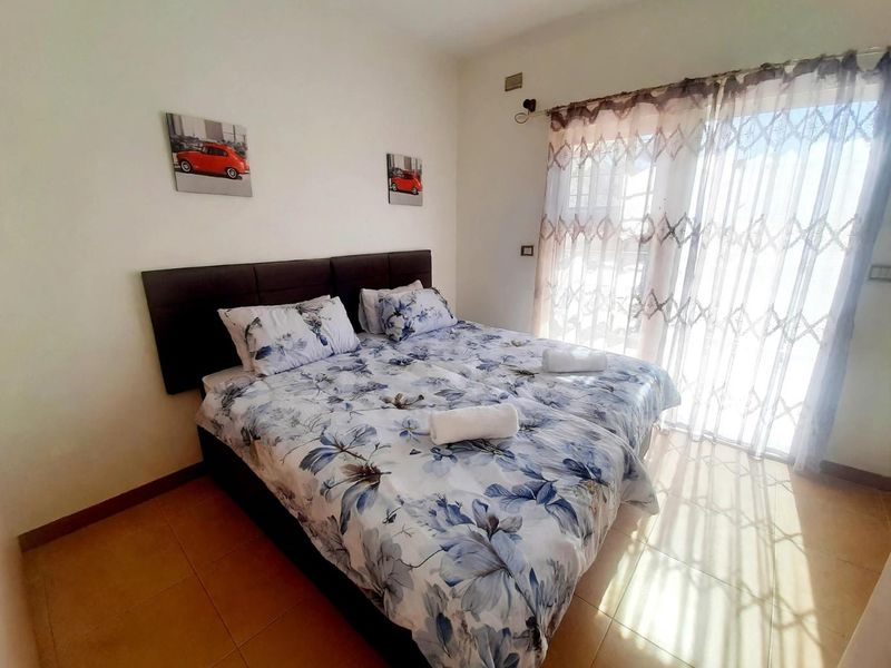 A functional bedroom featuring tiled flooring and a sliding glass door with an integrated security gate, providing natural light and access to the exterior.
