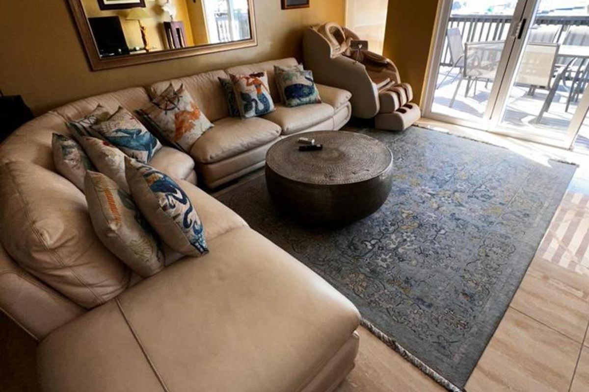 A comfortable living room featuring tiled flooring, a wall-mounted air conditioning unit, and sliding glass doors providing access to an outdoor patio area.