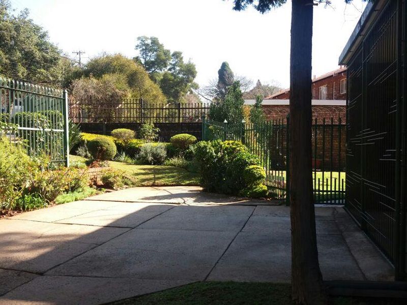 A private rear garden area featuring a paved patio, established landscaping, and secure perimeter steel fencing.