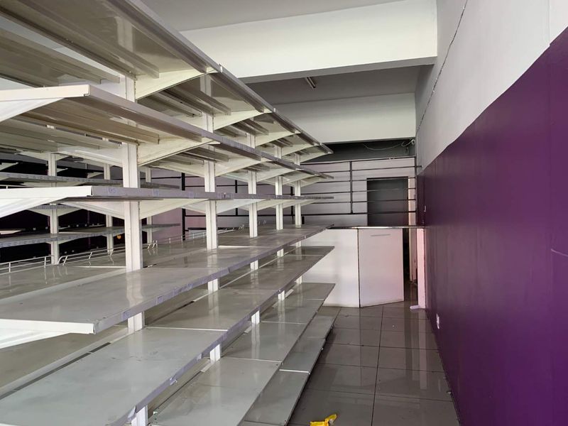 Open-plan retail space featuring fixed metal shelving units, tiled flooring, and painted walls, suitable for a variety of commercial business applications.