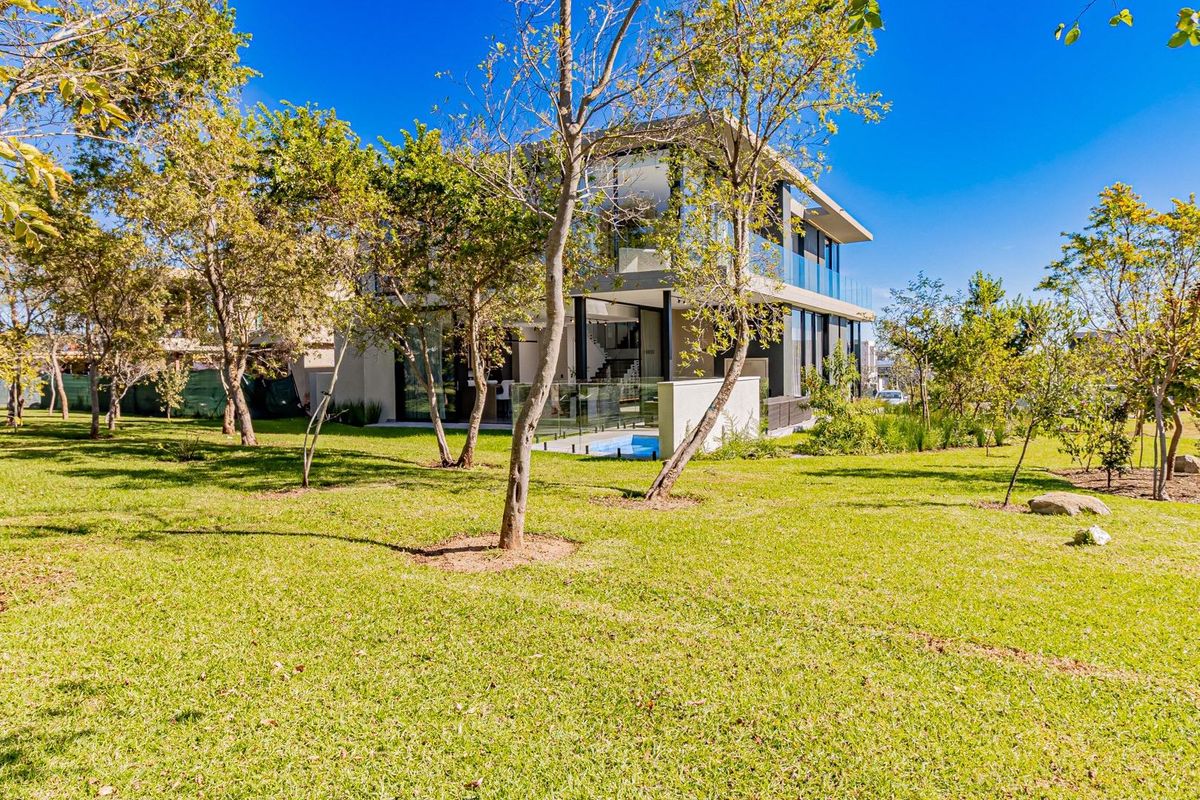 A modern multi-story residence featuring extensive glass facades, a balcony with glass balustrades, and a landscaped garden with a small pool.