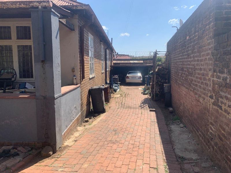 A side driveway leading to a rear carport, featuring brick paving and boundary walls with security fencing.