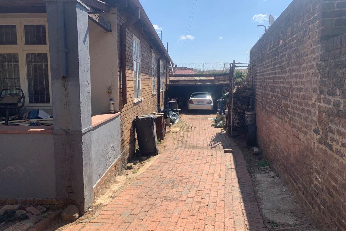 A side driveway leading to a rear carport, featuring brick paving and boundary walls with security fencing.
