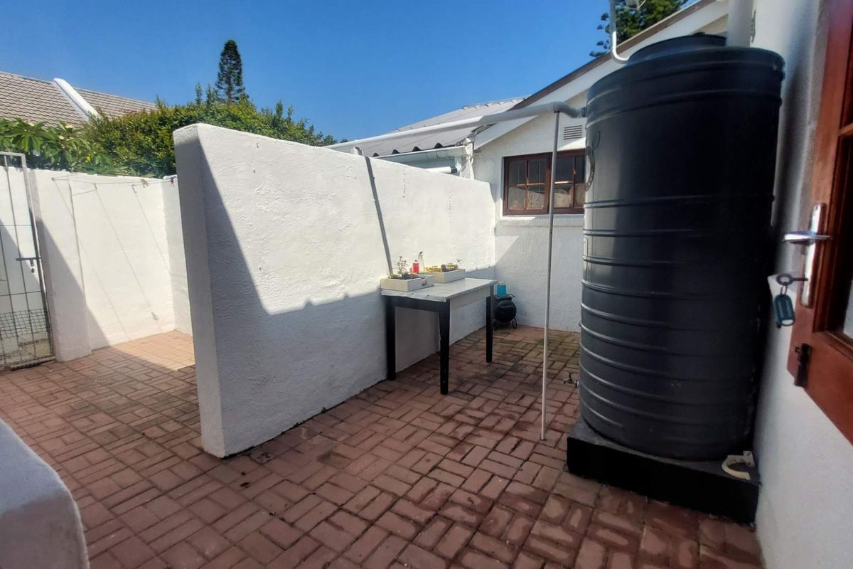 A private rear courtyard area featuring paved flooring, a privacy wall, and a large water storage tank.