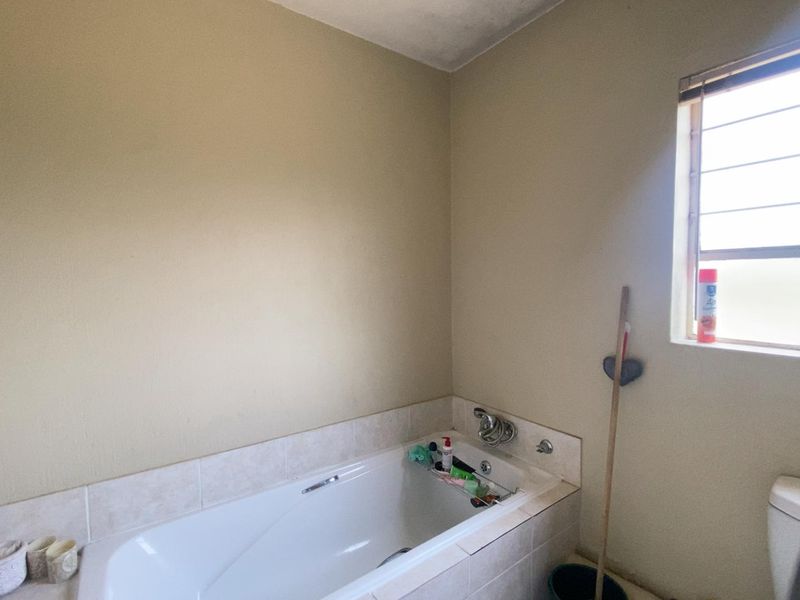 A functional bathroom featuring a built-in bathtub with tiled surround and a window with security bars, requiring some cosmetic updates to the walls and ceiling.