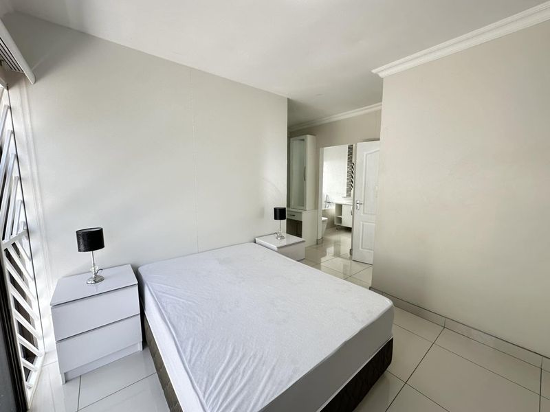 A bright bedroom featuring tiled flooring, crown molding, and direct access to an en-suite bathroom with a built-in vanity.
