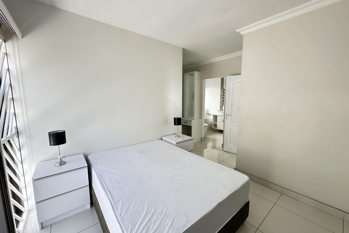A bright bedroom featuring tiled flooring, crown molding, and direct access to an en-suite bathroom with a built-in vanity.
