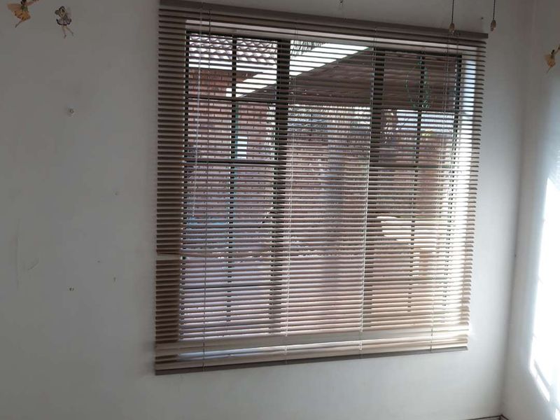 An empty bedroom featuring tiled flooring and venetian blinds, requiring minor cosmetic updates to the wall surfaces and window treatments.