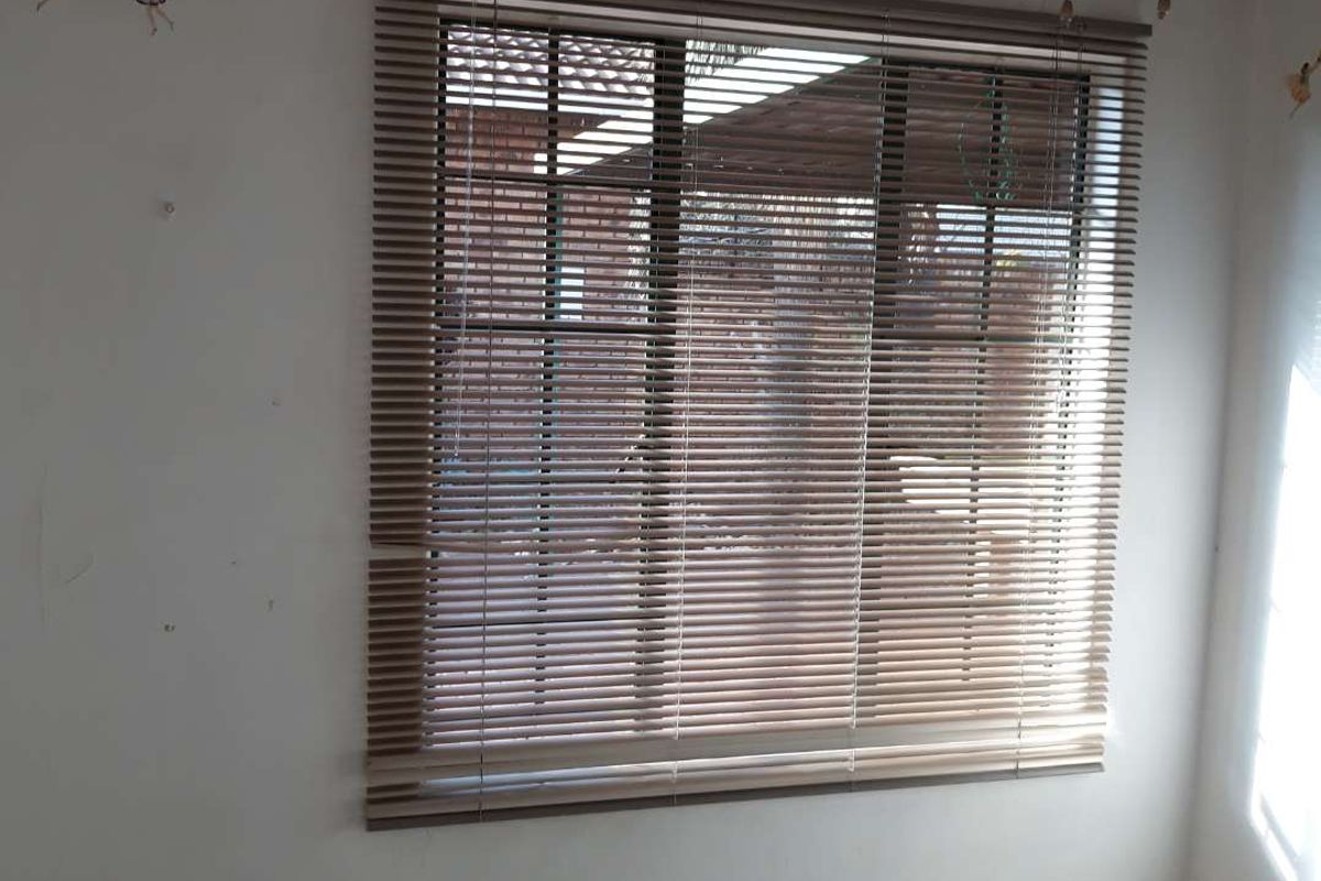 An empty bedroom featuring tiled flooring and venetian blinds, requiring minor cosmetic updates to the wall surfaces and window treatments.