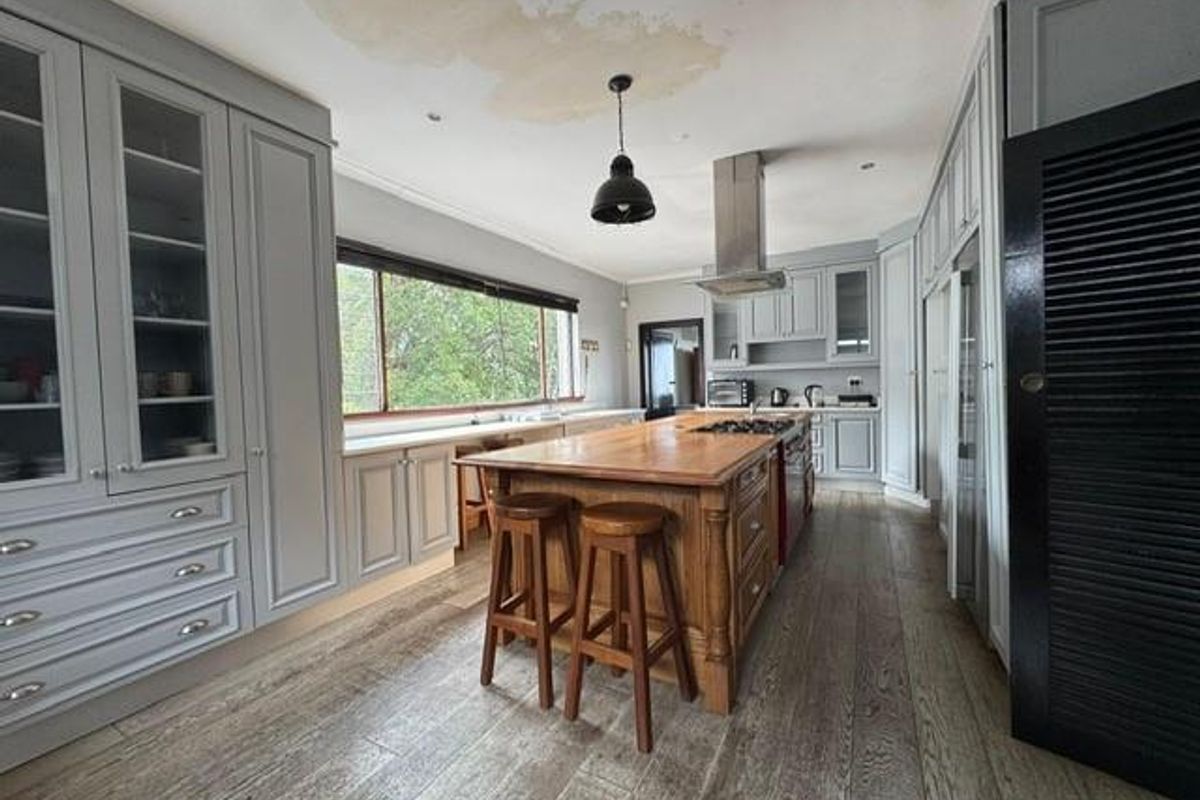 Spacious kitchen featuring custom cabinetry, a large central wooden island with integrated cooktop, stainless steel extractor fan, and wood-look flooring.