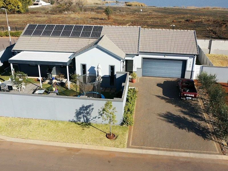 Aerial view of a residential property featuring a tiled roof with solar panels, a paved driveway, a garage, and a private enclosed garden area.