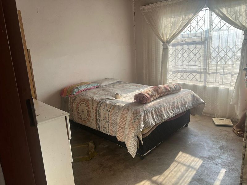 A bedroom featuring a window with a security gate and basic wall finishes, requiring cosmetic updates to improve the overall condition.