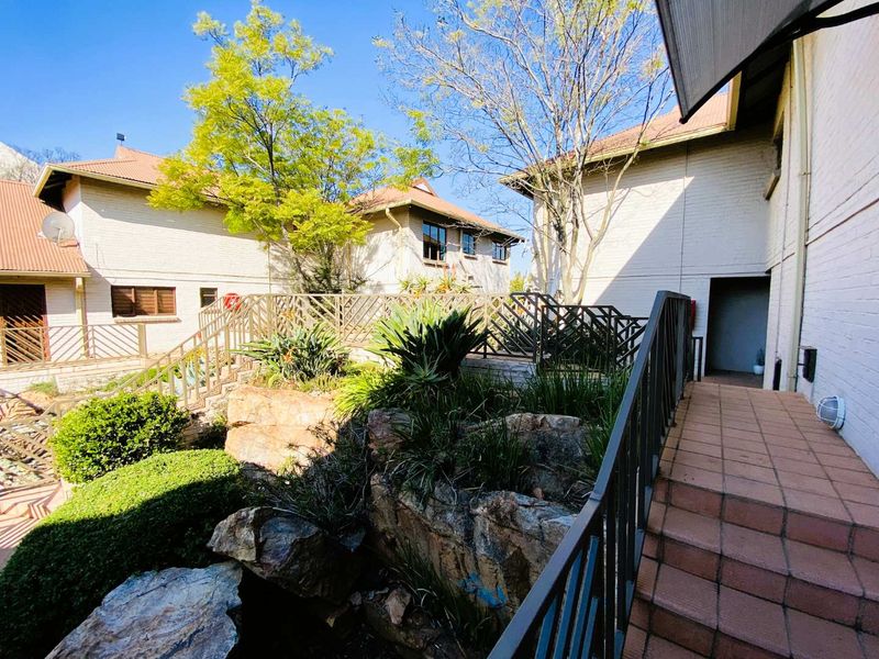 A well-maintained exterior rear courtyard area featuring a tiled staircase, metal railings, and established rock garden landscaping between townhouse units.