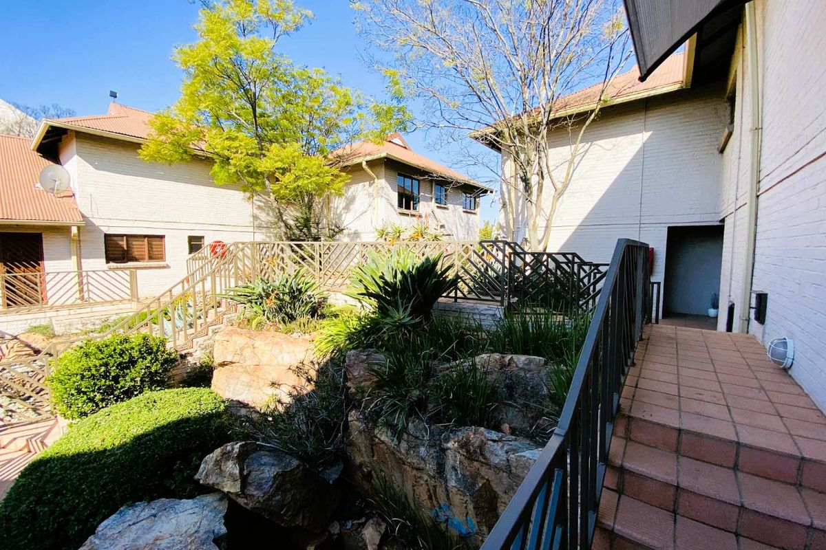 A well-maintained exterior rear courtyard area featuring a tiled staircase, metal railings, and established rock garden landscaping between townhouse units.