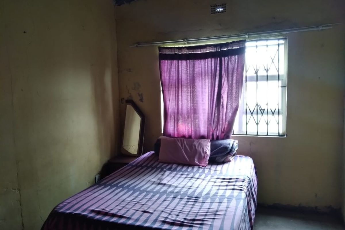 A bedroom featuring a window with security bars and basic wall finishes, requiring cosmetic updates and maintenance.