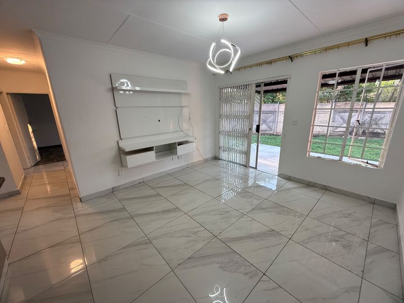 Bright living room featuring polished marble-look floor tiles, a built-in media console, and direct access to the rear patio through a sliding glass door.