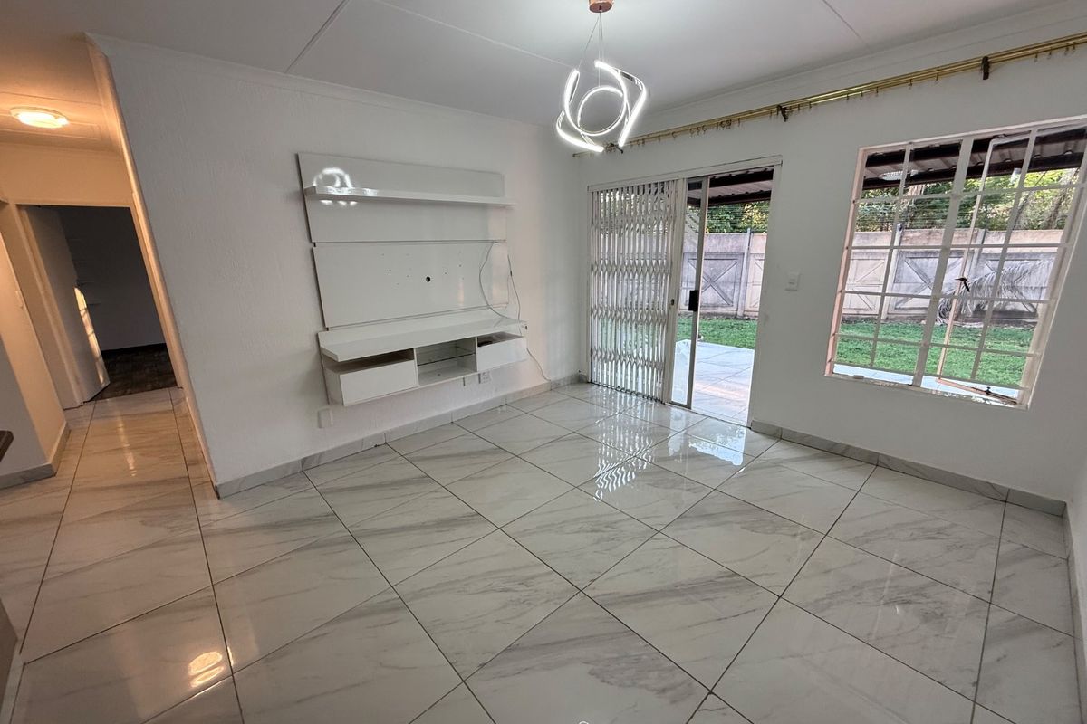 Bright living room featuring polished marble-look floor tiles, a built-in media console, and direct access to the rear patio through a sliding glass door.