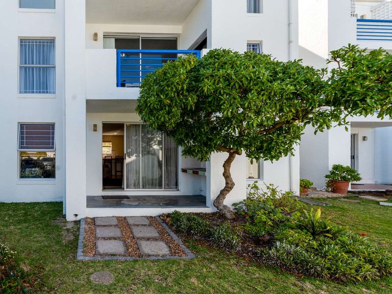 Ground floor apartment exterior featuring a private patio with a built-in braai, sliding door access, and a well-maintained garden area.