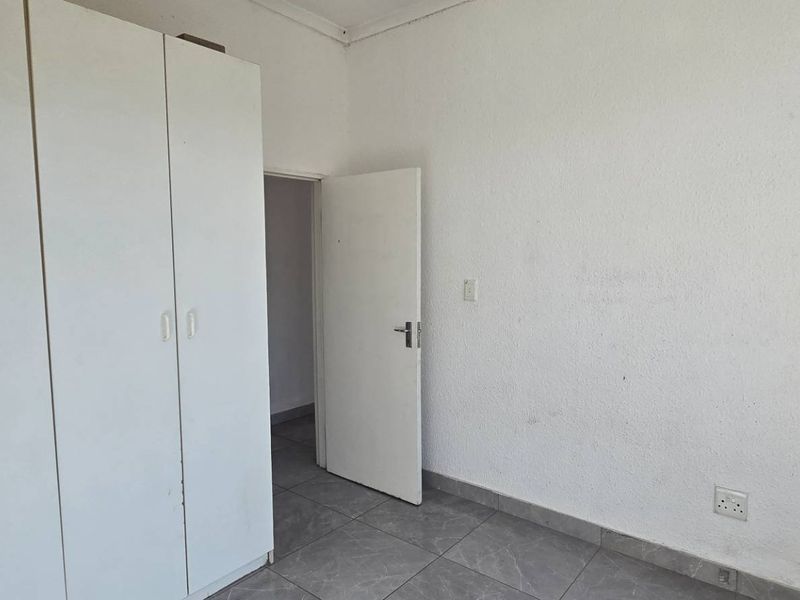 A simple bedroom featuring tiled flooring and built-in cupboards, offering a clean and functional space ready for personalization.
