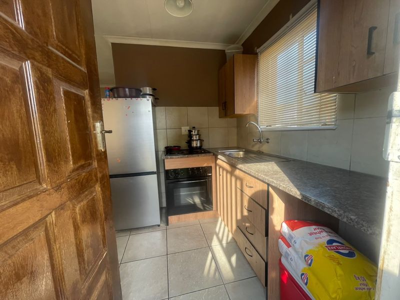 A compact kitchen featuring built-in cabinetry, laminate countertops, a stainless steel sink, and a built-in oven with hob, finished with tiled flooring and backsplash.