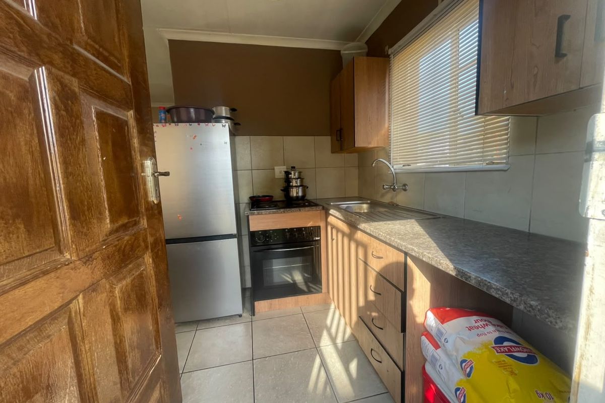 A compact kitchen featuring built-in cabinetry, laminate countertops, a stainless steel sink, and a built-in oven with hob, finished with tiled flooring and backsplash.