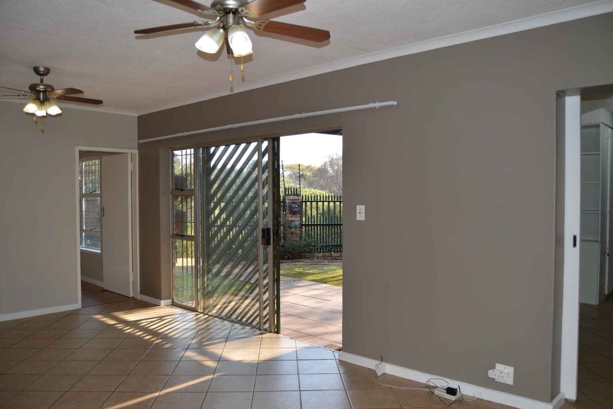 Spacious living area featuring ceramic floor tiles, dual ceiling fans, and a sliding glass door providing direct access to the rear patio and garden.