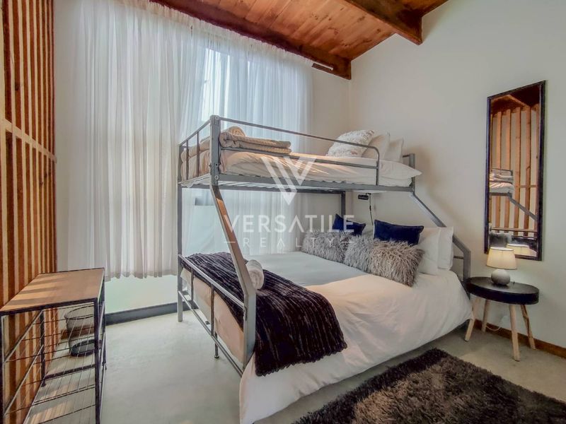 A cozy bedroom featuring exposed timber ceiling beams, polished concrete flooring, and a large window allowing for ample natural light.