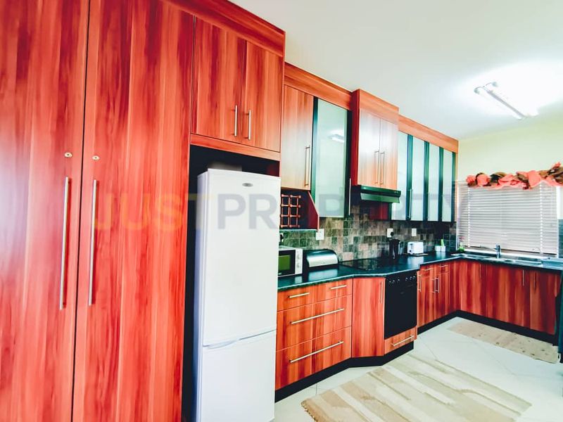 A functional kitchen featuring wood-grain cabinetry, dark laminate countertops, a tiled backsplash, and integrated cooking appliances.