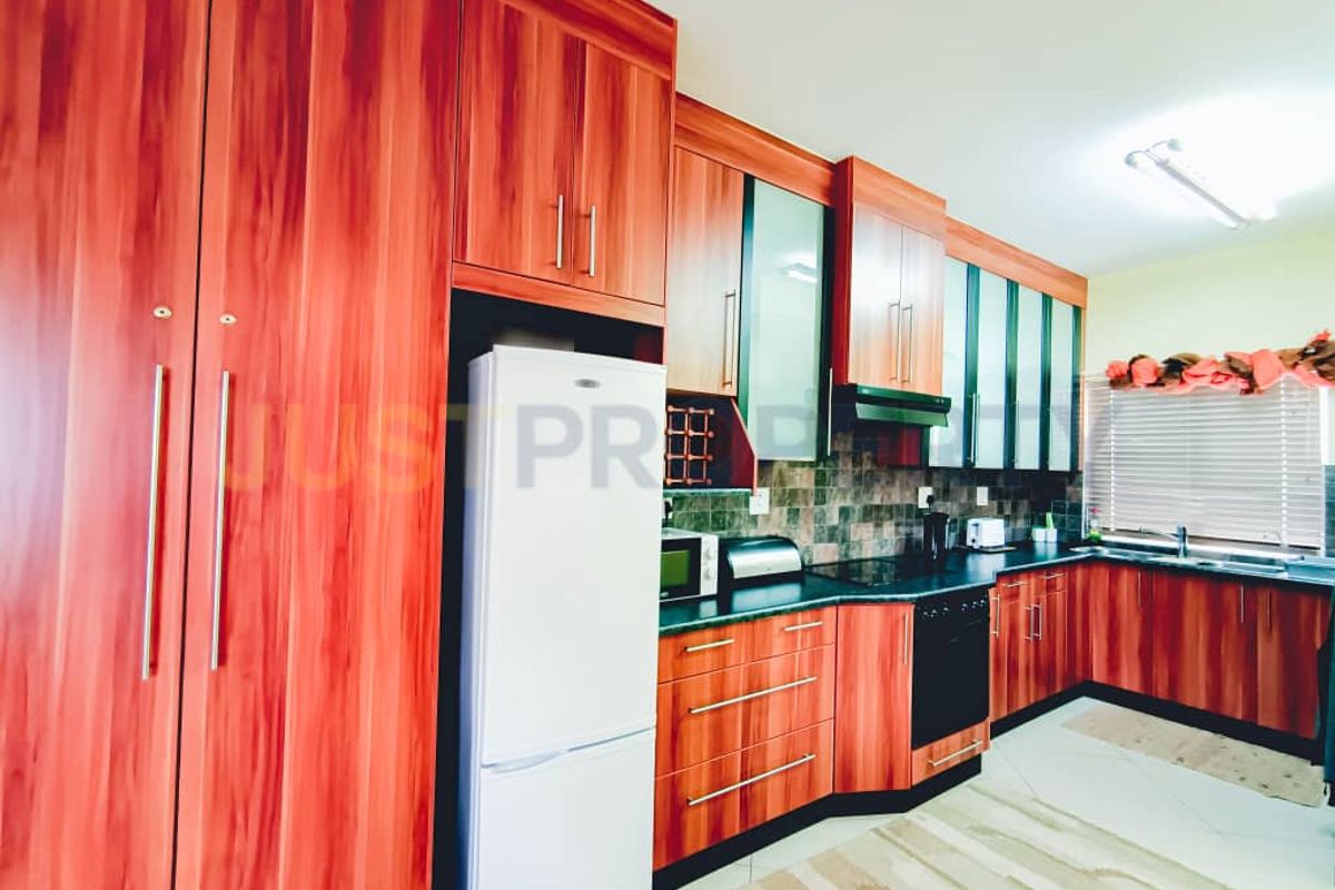 A functional kitchen featuring wood-grain cabinetry, dark laminate countertops, a tiled backsplash, and integrated cooking appliances.