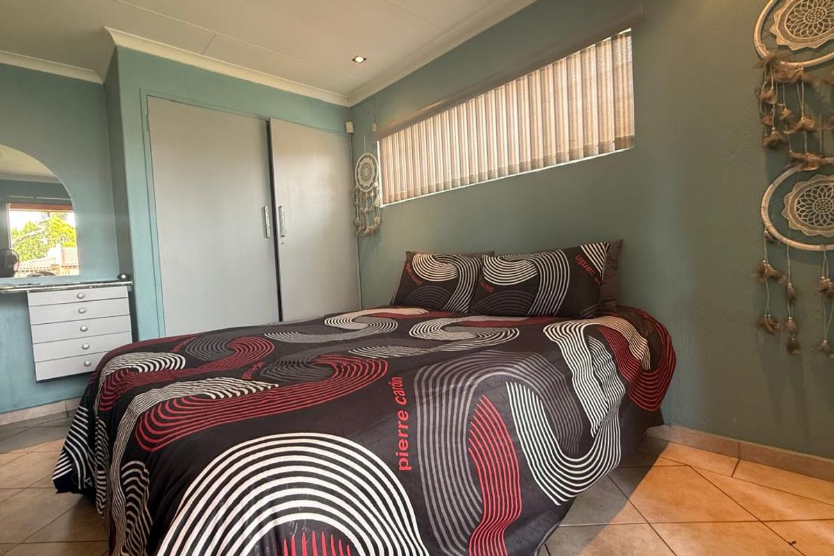 A bedroom featuring built-in cupboards, tiled flooring, and a horizontal window with fitted blinds.
