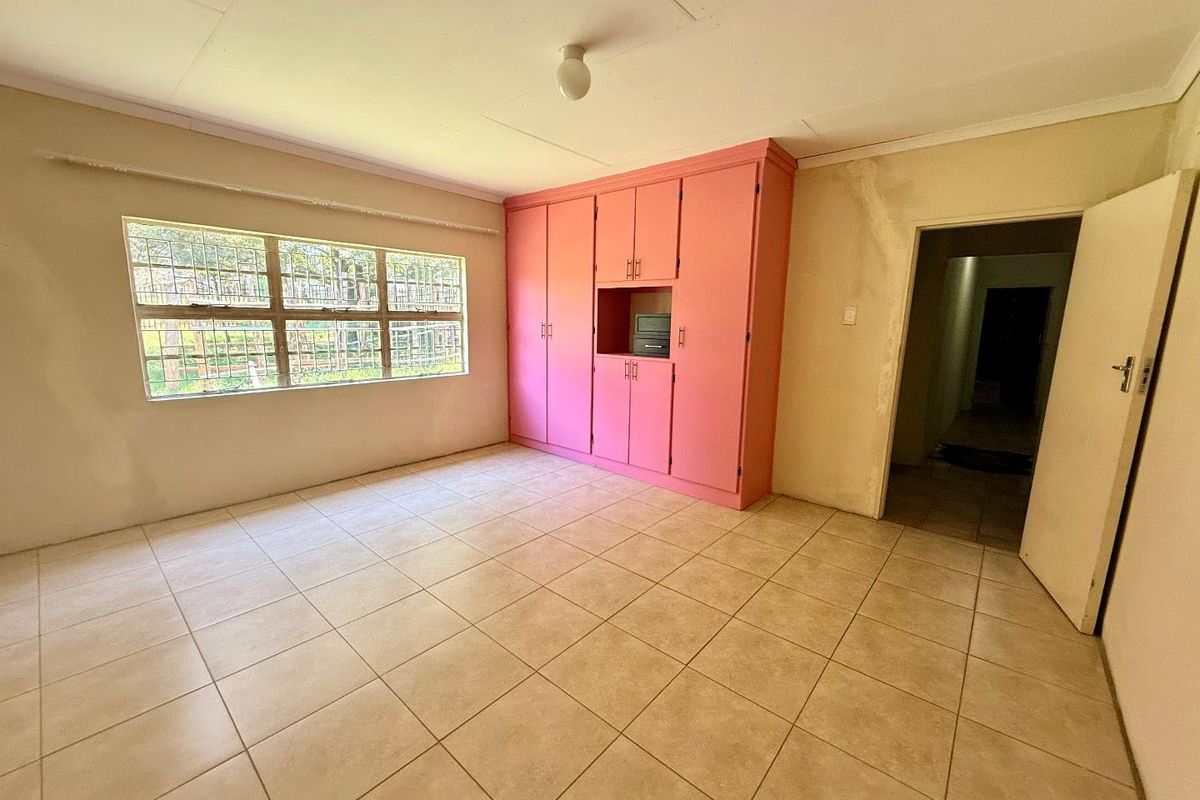 A vacant bedroom featuring tiled flooring, built-in pink cabinetry, and a large window, requiring cosmetic updates to the walls and ceiling.