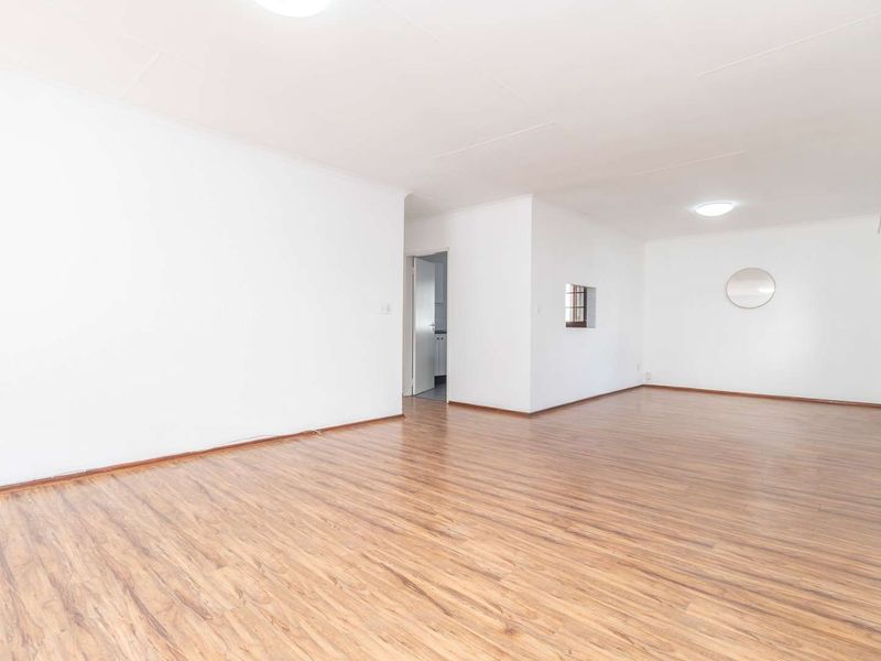 A bright, empty living room featuring laminate wood-look flooring and neutral white walls, offering a clean and versatile space ready for personalization.