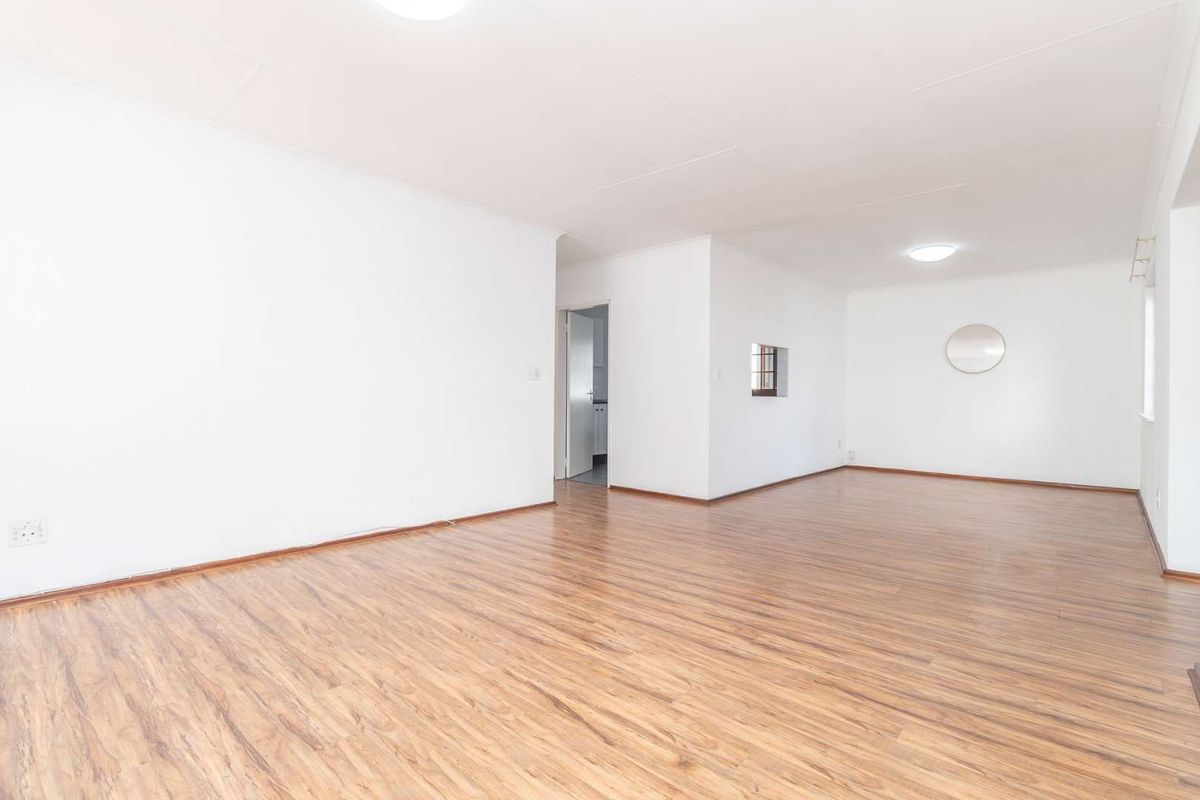 A bright, empty living room featuring laminate wood-look flooring and neutral white walls, offering a clean and versatile space ready for personalization.
