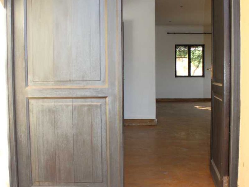 Entrance view into an apartment featuring double timber doors and open-plan living space with concrete flooring.