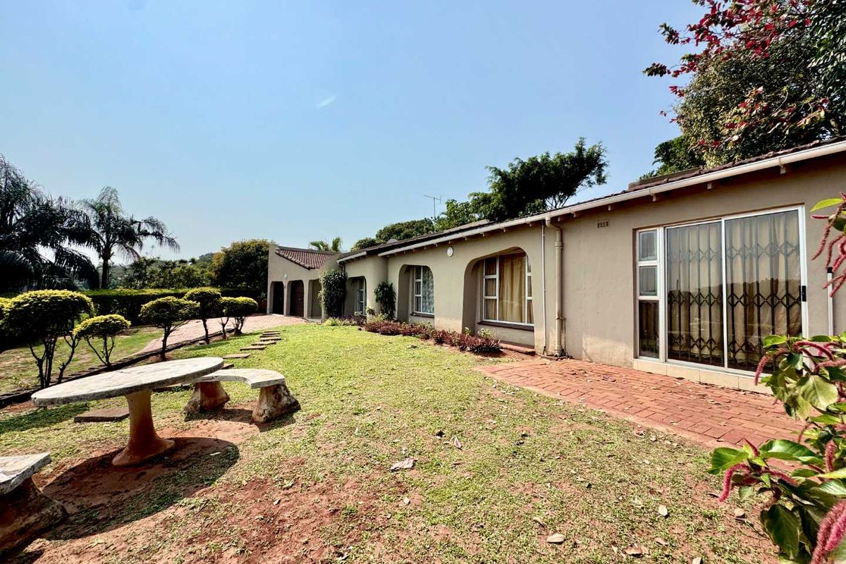 Rear view of the house featuring a brick paved patio, sliding glass doors with security gates, and a spacious garden area.