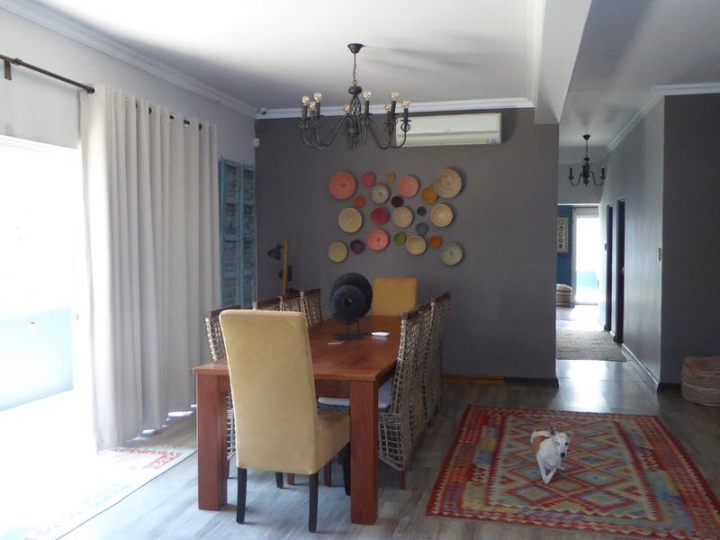 A well-lit dining area featuring laminate flooring, a decorative chandelier, and a wall-mounted split-system air conditioner, providing a comfortable space for meals.