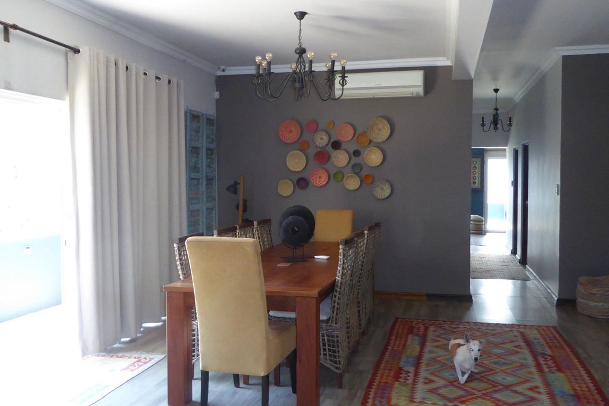 A well-lit dining area featuring laminate flooring, a decorative chandelier, and a wall-mounted split-system air conditioner, providing a comfortable space for meals.